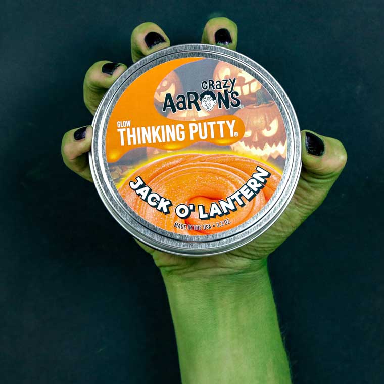 Green hand holding a tin of Crazy Aaron's Jack O Lantern Thinking Putty®.