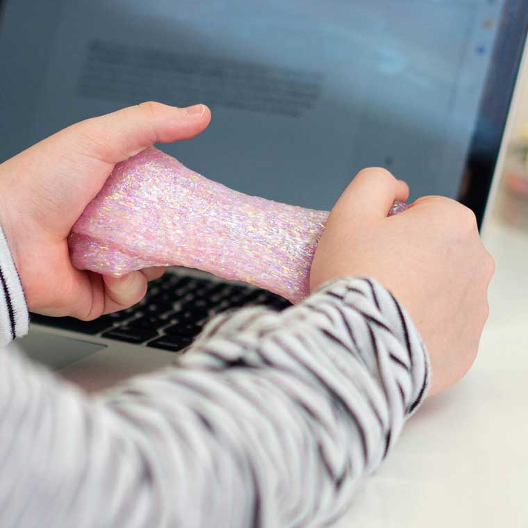 Two hands on a table with a laptop holding pink sparkle putty.