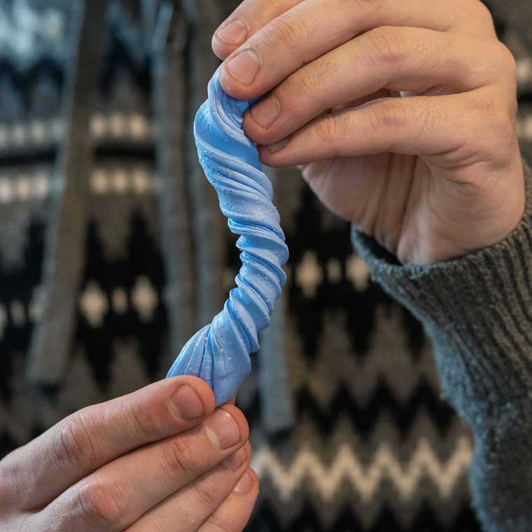 Two hands twisting blue, hot cocoa scented Thinking Putty®.